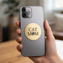 A round, brushed gold metal sticker featuring the text 'CAT MOM' in black, with the letter 'O' replaced by a black paw print icon, shown on a plain white background.