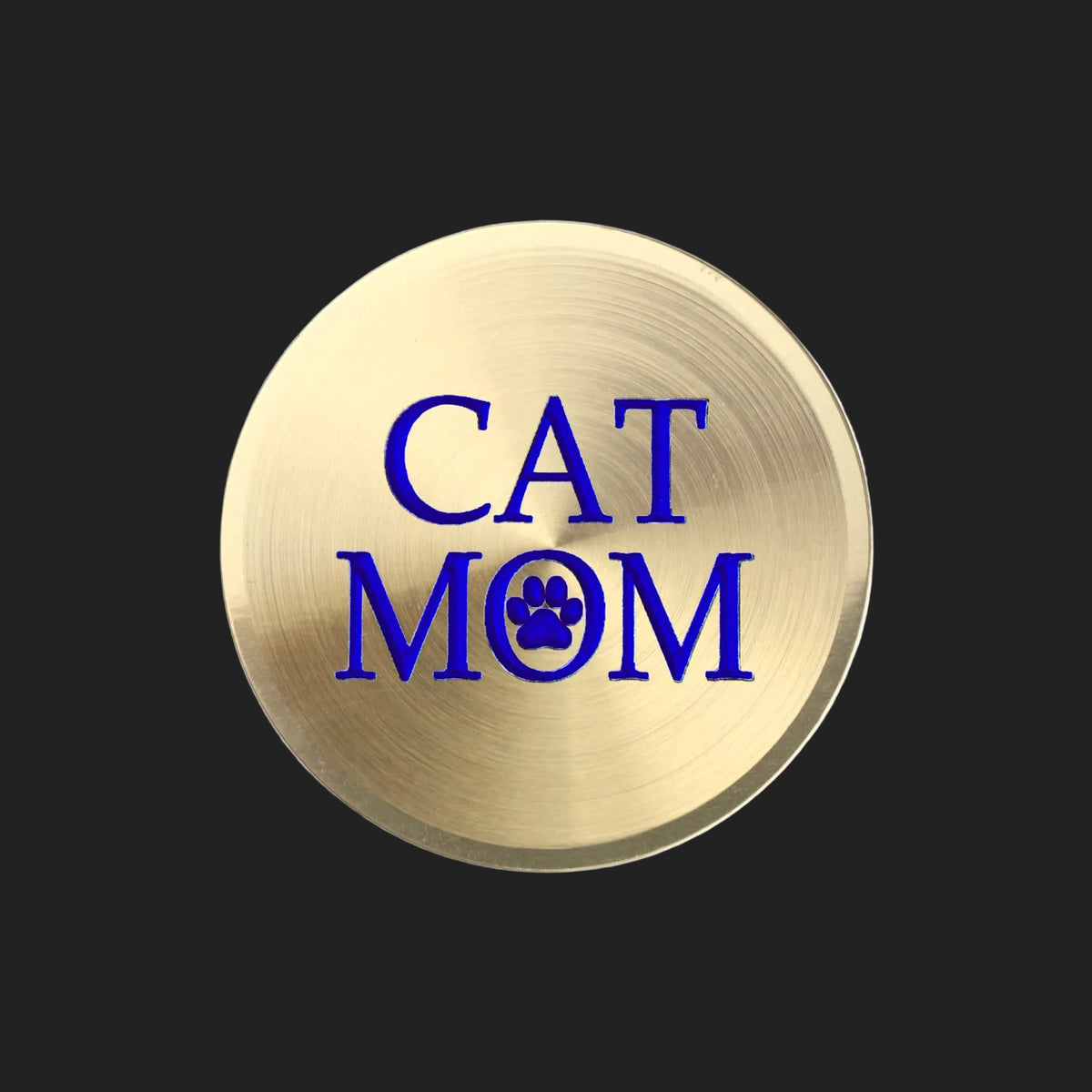 A round, brushed gold metal sticker featuring the text 'CAT MOM' in bold blue lettering, with a blue paw print icon replacing the letter 'O' in 'MOM', set against a plain white background.