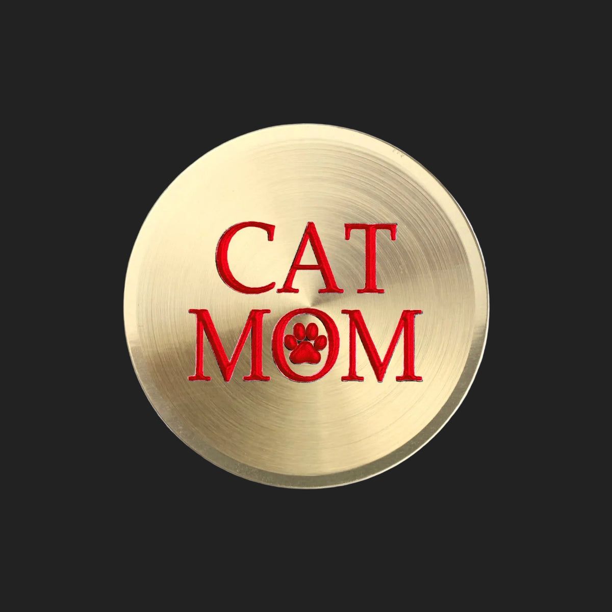 A round, brushed gold metal sticker featuring the text 'CAT MOM' in red, with the letter 'O' replaced by a red paw print icon, shown on a plain white background.