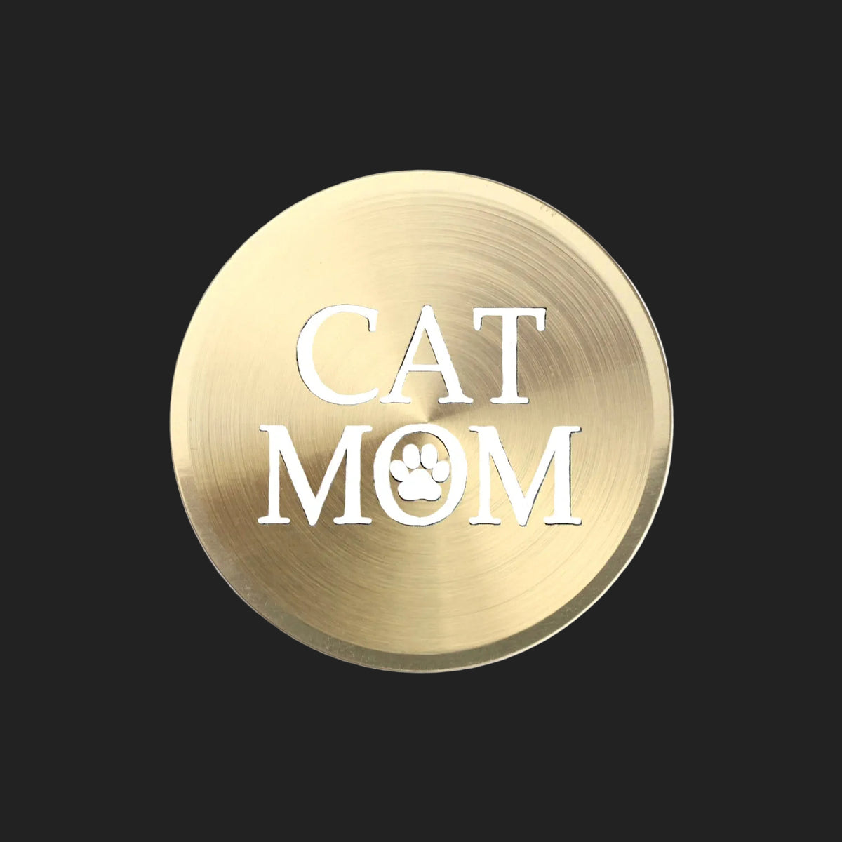 A round, brushed gold metal sticker featuring the text 'CAT MOM' in white, with the letter 'O' replaced by a white paw print icon, shown on a plain white background.