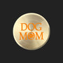 A round, brushed gold metal sticker featuring the words 'DOG MOM' in orange lettering with a paw print icon, set against a plain white background.