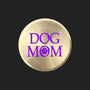 A round, brushed gold metal button or badge featuring the text 'DOG MOM' in purple, with the letter 'O' replaced by a purple paw print icon, shown on a plain white background.