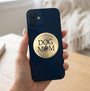 A round, brushed brass or gold-colored metal sign with the words 'DOG MOM' in black lettering and a black paw print icon, shown on a plain white background.
