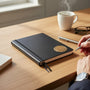 Metal Stickems 2-inch bronze laurel wreath adhesive emblem applied to a black notebook on a wooden desk