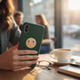 Metal Stickems circular gold-tone metal sticker with crossed American flags applied to a green smartphone case.