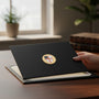 Metal Stickems Episcopal Shield emblem in gold-tone with red and blue details applied to a black folder on a desk.