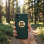 Metal Stickems 2-inch gold and black U.S. Forest Service metal sticker on a green phone case in a forest setting.