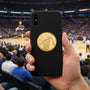 Metal Stickems gold basketball hoop emblem sticker applied to a black smartphone case in a stadium setting.