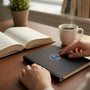 Metal Stickems religious cross emblem in gold and blue applied to a black notebook on a desk with coffee and a book.