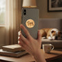 Metal Stickems gold bulldog round metal emblem sticker applied to the back of a smartphone held by a hand.