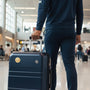 Metal Stickems gold football emblem applied to a navy blue suitcase held by a traveler in an airport terminal.