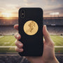 Metal Stickems gold football player metal sticker applied to a black smartphone case with a stadium background.