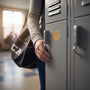 Metal Stickems gold hockey emblem sticker applied to a grey school locker door with a person holding a sports bag.
