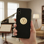 Metal Stickems gold lyre musical instrument emblem sticker applied to a black smartphone case in a music room.