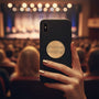 Metal Stickems round gold musical notation sticker applied to a black smartphone case in a concert hall setting.