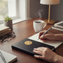 Metal Stickems gold religious handshake sticker on a black notebook held by a person writing at a desk.