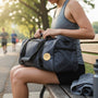 Metal Stickems gold running couple emblem applied to a grey gym duffel bag held by a woman sitting on a park bench.