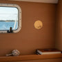 Metal Stickems 2-inch round gold embossed sailboat sticker applied to a wooden cabin wall near a porthole.