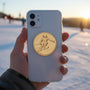 Metal Stickems gold-toned alpine skier metal sticker applied to the back of a white smartphone against a snowy backdrop