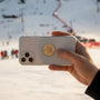 Metal Stickems gold skier emblem sticker applied to the back of a smartphone with a snowy ski slope background.