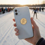 Metal Stickems gold embossed skier metal sticker applied to a smartphone case with a snowy ski track background.