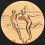 Metal Stickems 2-inch gold-toned adhesive emblem featuring a high-relief embossed design of two soccer players.