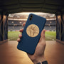 Metal Stickems gold-toned soccer player metal sticker applied to a navy blue smartphone case in a stadium setting.