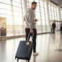 Metal Stickems gold soccer player emblem sticker applied to a black suitcase held by a man in an airport terminal.