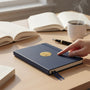 Metal Stickems gold swimming competition medallion sticker applied to a blue notebook on a desk with books and coffee.