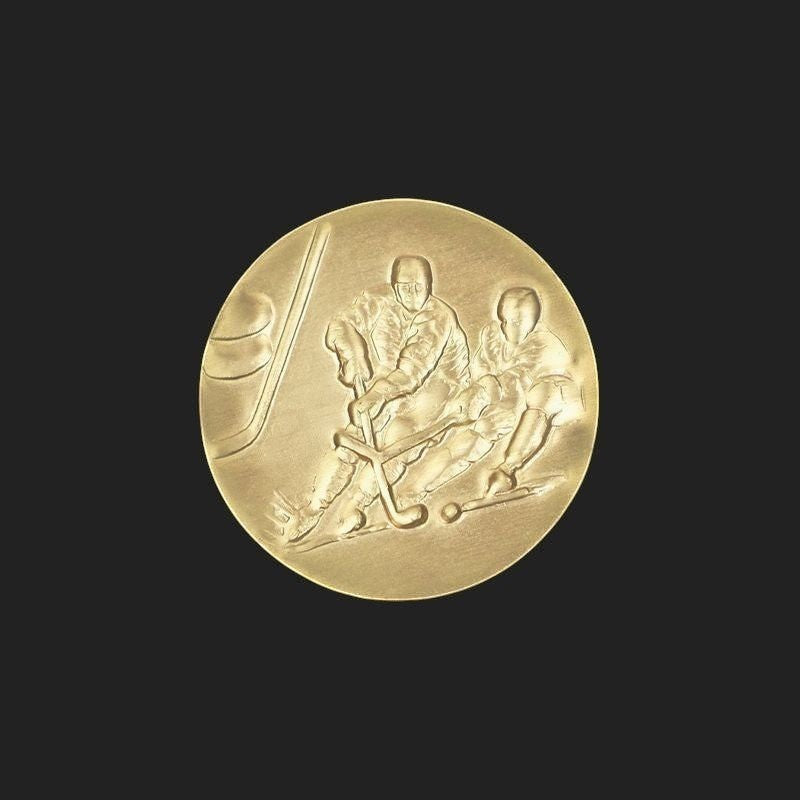 Metal Stickems gold-tone 1-inch ice hockey emblem sticker featuring an embossed action scene of hockey players.