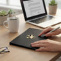 Metal Stickems religious symbol sticker with gold cross and prayer hands on a black notebook held by a person