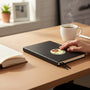 Metal Stickems 2-inch round gold-tone sticker with red heart and handshake design applied to a black notebook.