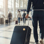 Metal Stickems rowing athlete decal on a black suitcase being pulled by a traveler in an airport terminal.