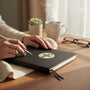 Metal Stickems 2-inch Outstanding Safety Record sticker with a green cross on a black notebook on a wooden desk.