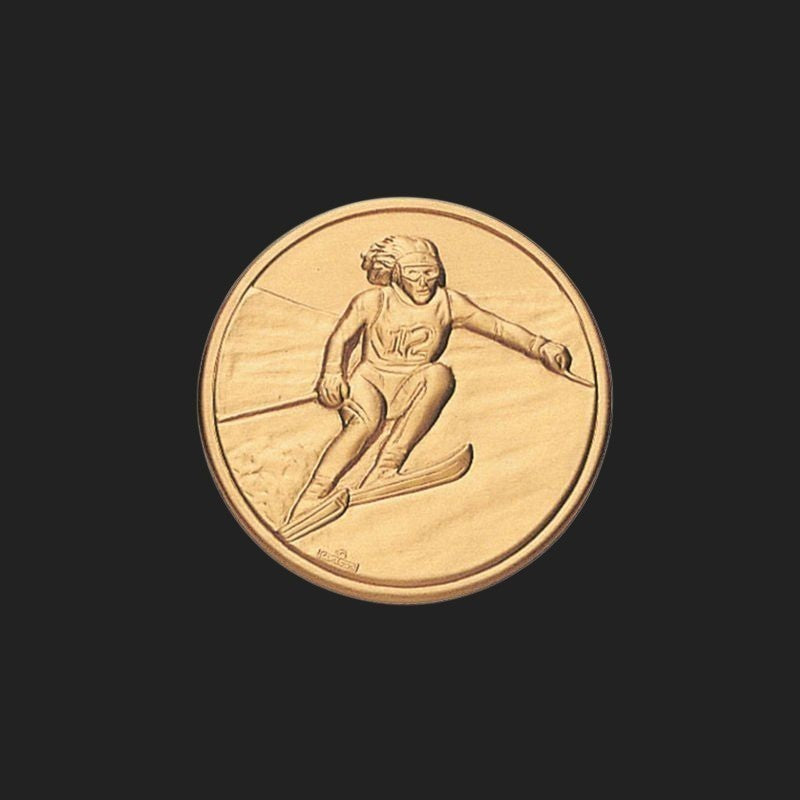 Metal Stickems 1-inch gold-tone embossed metal sticker featuring a detailed skier in motion for gear personalization.