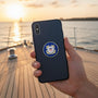 Metal Stickems 2-inch United States Coast Guard metal emblem sticker applied to a black smartphone case on a boat deck.